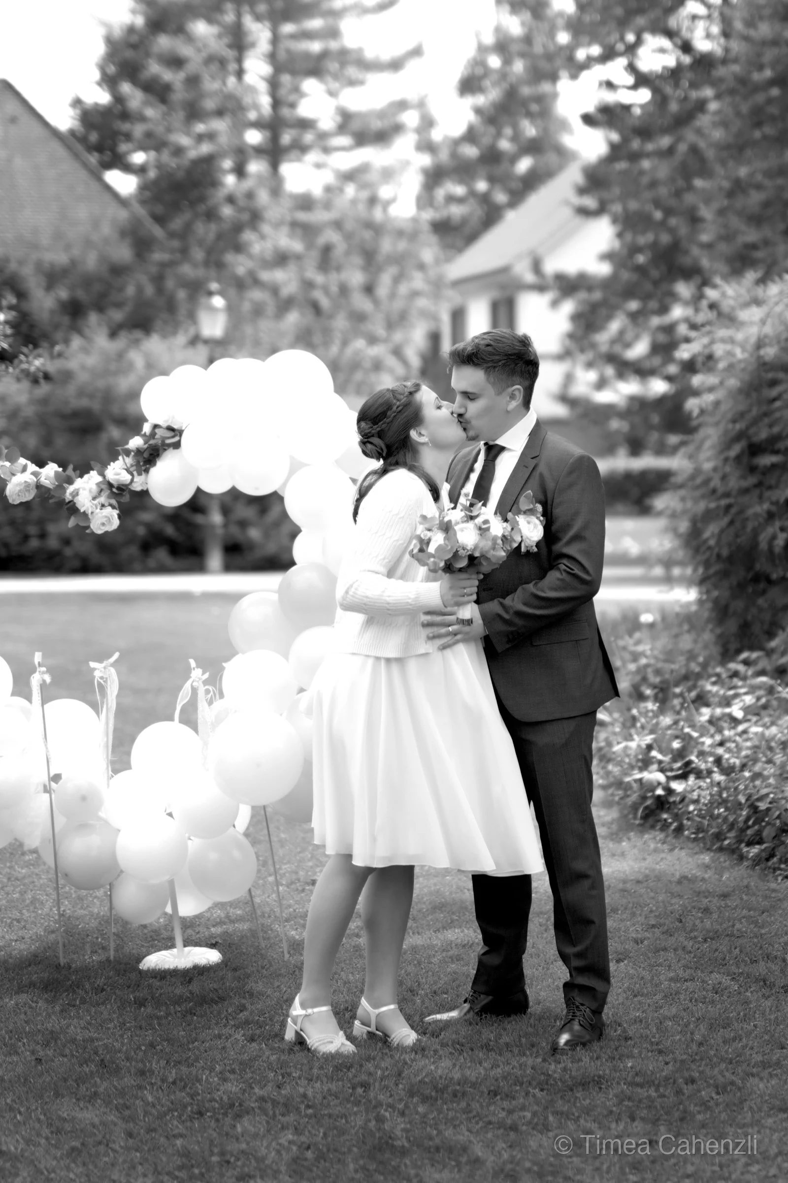 Brautpaar küsst sich im Garten mit weissen Luftballons – Schwarzweiss Hochzeit